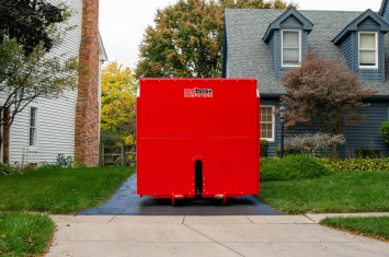 red dumpster in residential driveway in front of blue house