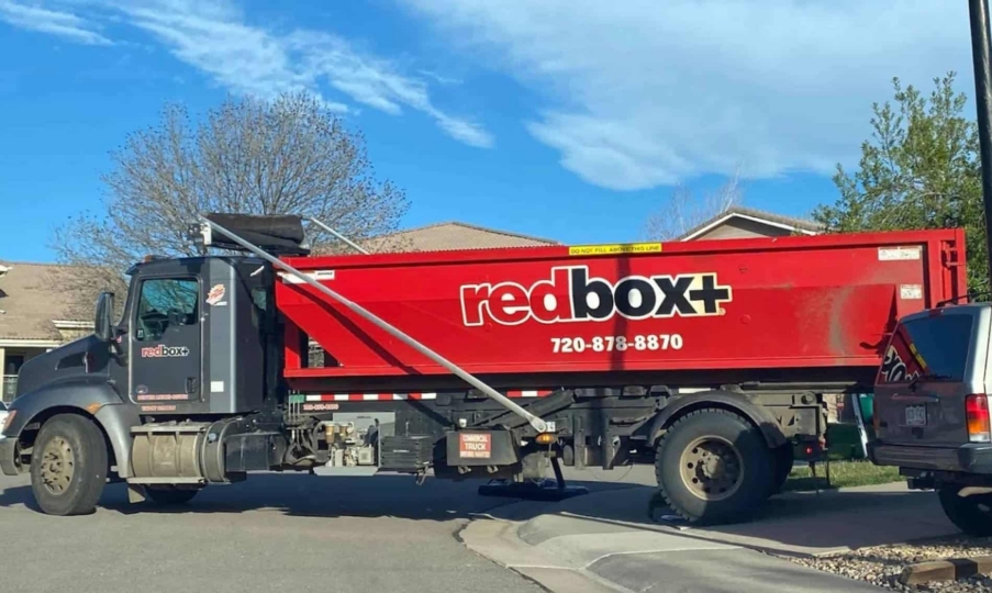 redbox+ Dumpsters of Denver South Metro truck providing roll-off dumpster hauling service in a residential neighborhood.