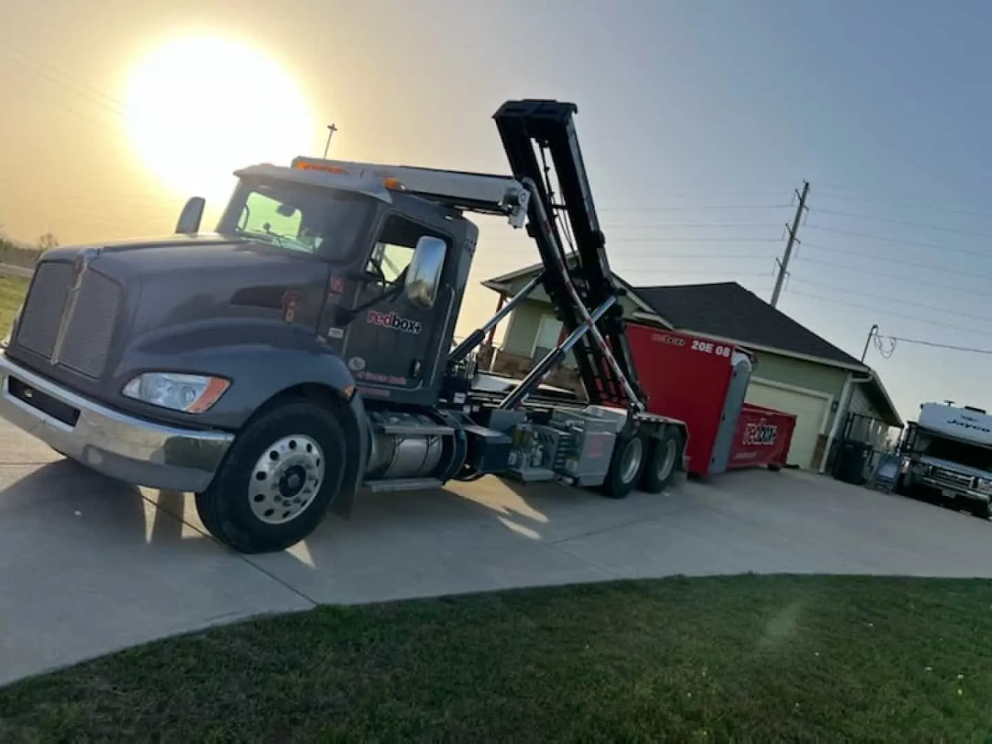 redbox+ roll-off truck delivering a dumpster to a home