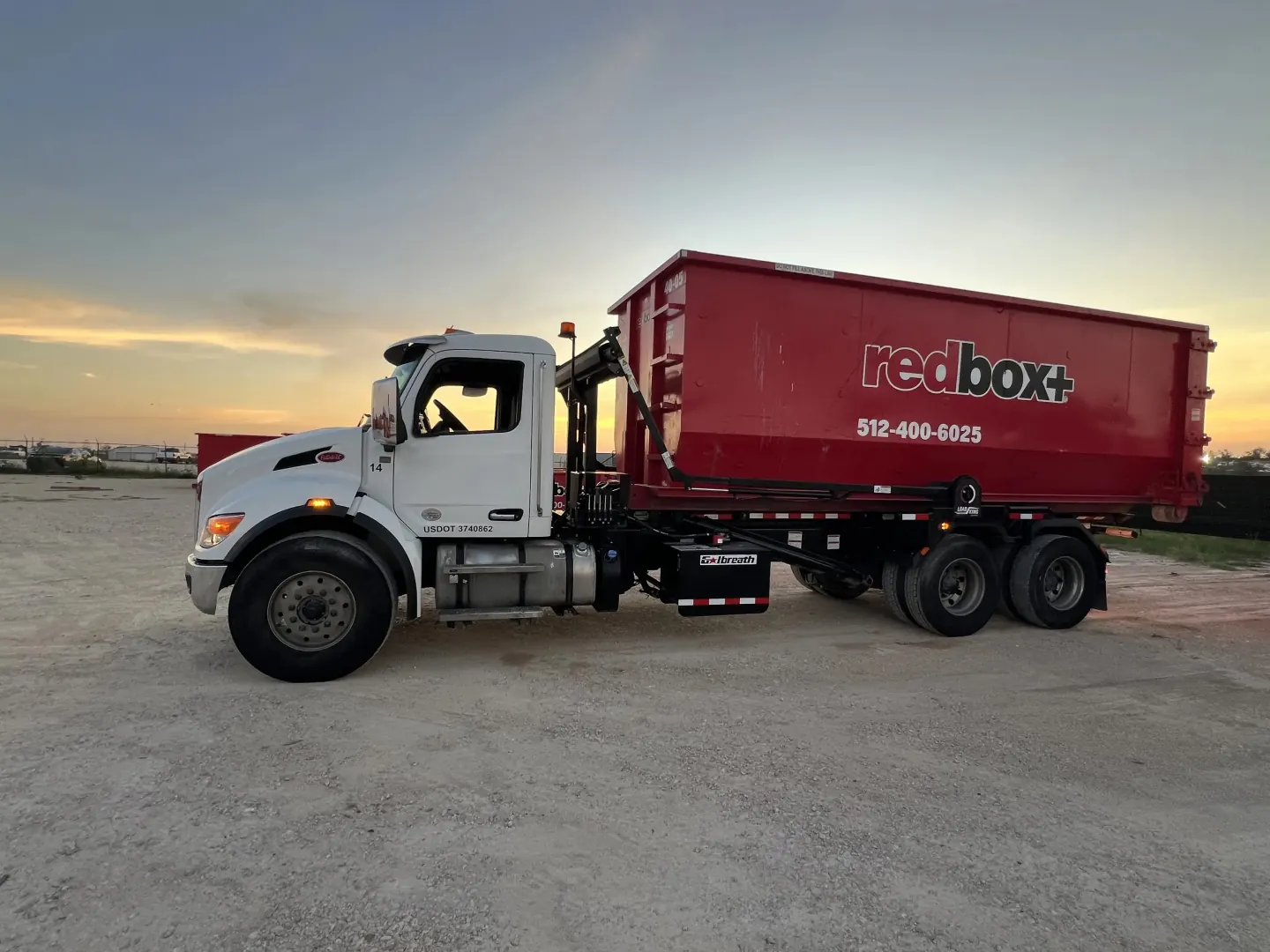 redbox+ roll-off truck carrying a dumpster