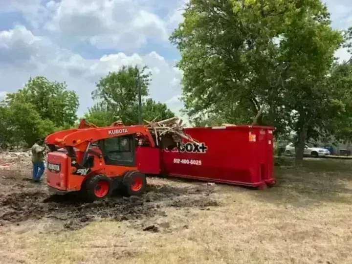 Skid steer loading a redbox+ dumpster during land clearing