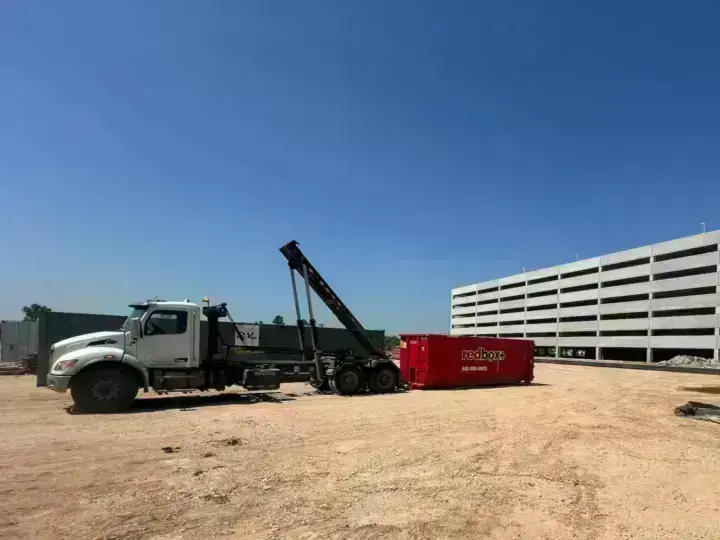 redbox+ truck placing a dumpster near a parking garage construction site