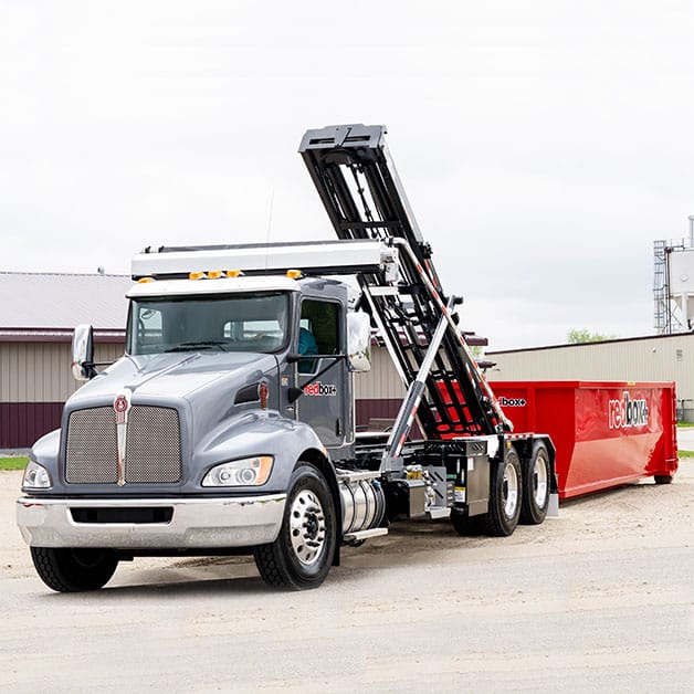 Roll-off truck carrying a red dumpster