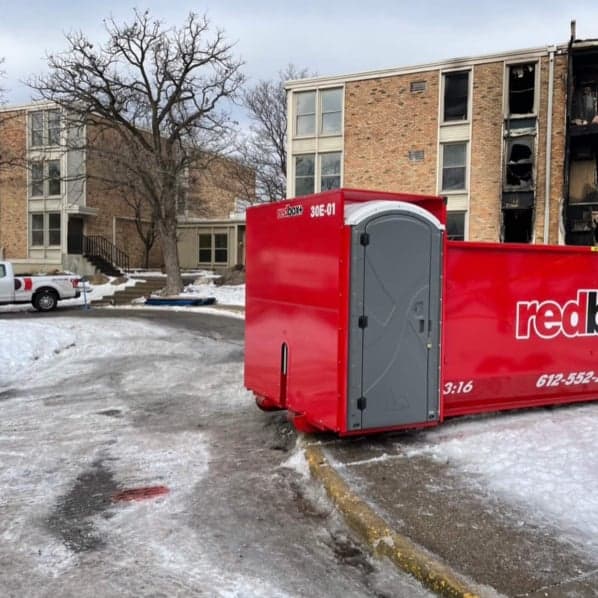 redbox+ dumpster rental in icy parking lot with burned building behind