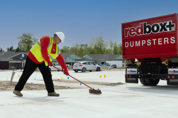 redbox+ Dumpsters employee sweeping driveway next to dumpster