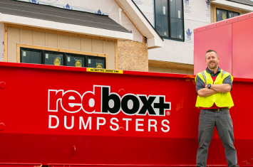 Two men wearing yellow vests standing in front of a redbox+ dumpster rental